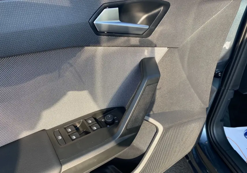 Gros plan sur la porte côté conducteur d'une SEAT Leon gris magnetic, montrant les commandes des vitres et le revêtement texturé.
