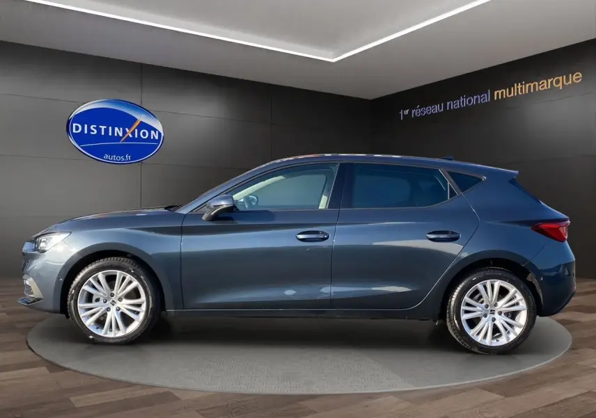 Vue latérale côté gauche d'une SEAT Leon IV gris magnetic avec jantes alu 17 pouces dans un showroom.