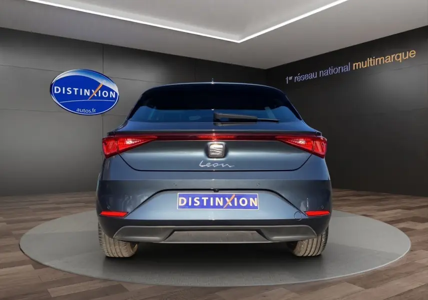 Vue arrière d'une SEAT Leon IV gris magnetic, avec feux LED et logo distinctif sur fond d'intérieur showroom.