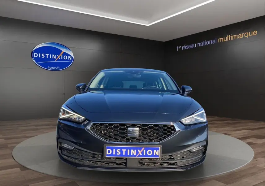 Vue frontale d'une SEAT Leon IV gris magnetic avec phares LED et calandre hexagonale en showroom.