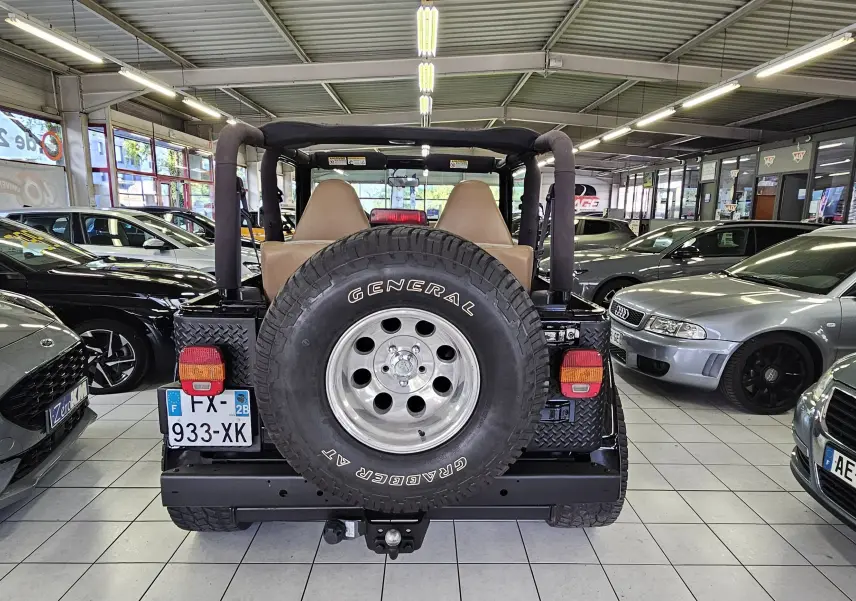 Vue arrière d'une Jeep Wrangler noire de 2000 avec roue de secours General Grabber et intérieur beige visible.