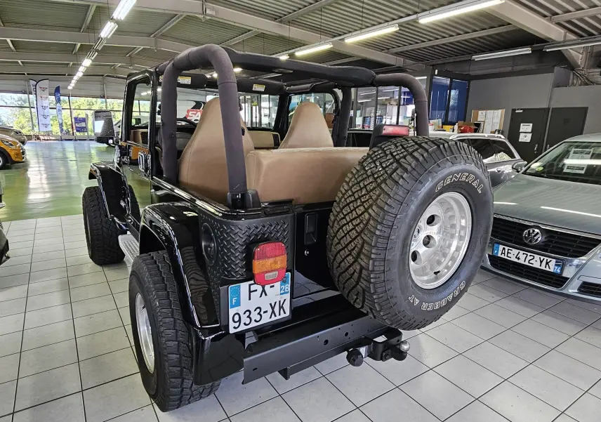 Vue arrière droite d'un Jeep Wrangler noir de 2000 avec roue de secours et intérieur beige en showroom.