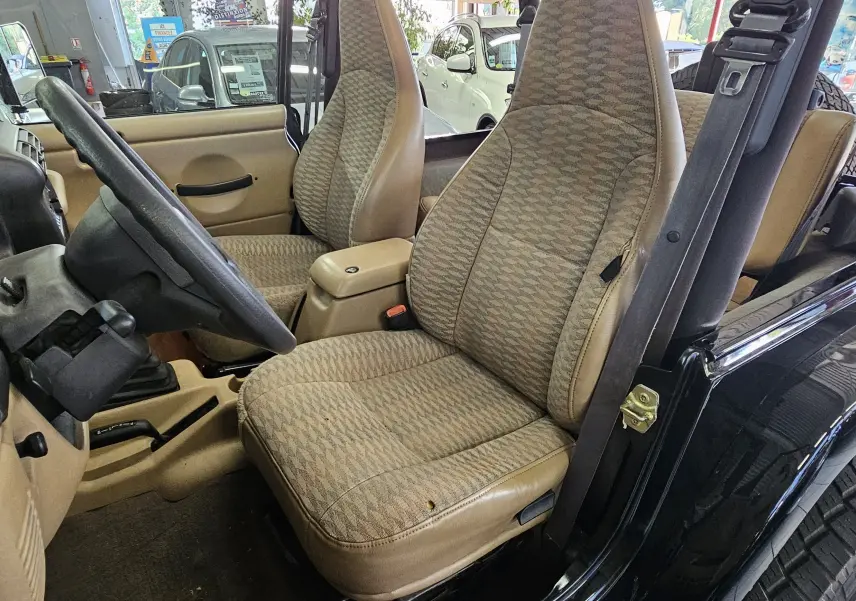 Intérieur beige du Jeep Wrangler 2000 vu côté conducteur, avec sièges en tissu à motifs et tableau de bord simple.