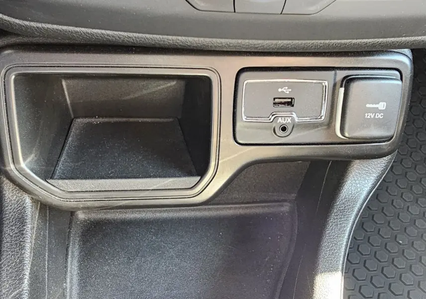 Gros plan sur la console centrale du Jeep Renegade 2020 montrant prise USB, AUX et prise 12V sur tapis caoutchouc noir.