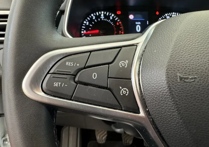 Gros plan sur les commandes du régulateur de vitesse à gauche du volant noir de la Renault Clio Business blanche de 2021.