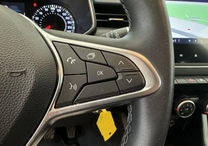 Gros plan sur les commandes du volant côté droit de la Renault Clio Business blanche, avec écran tactile et tableau de bord visible.