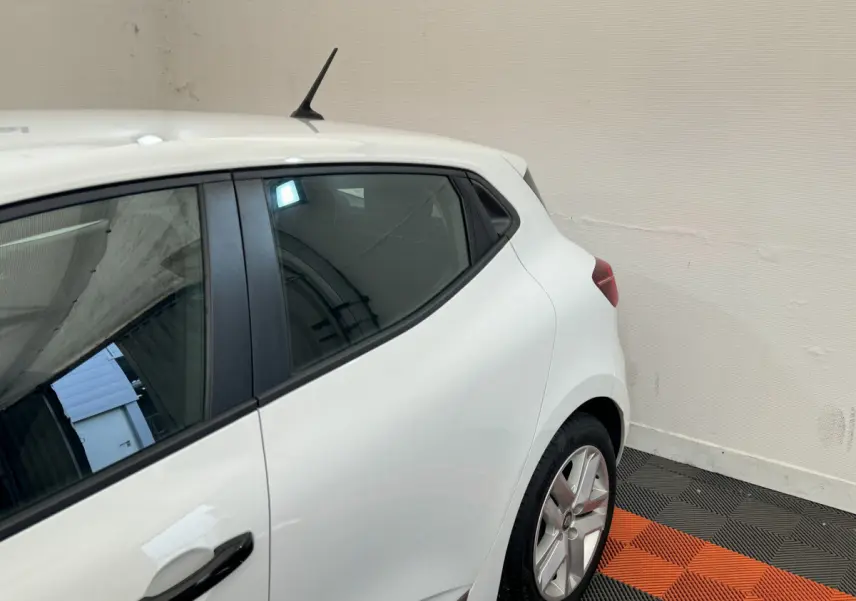 Vue côté gauche arrière d'une Renault Clio Business blanche avec poignées de porte noires et jantes alliage.