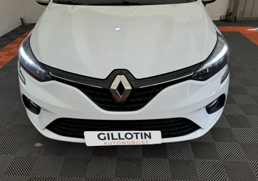 Vue frontale rapprochée d'une Renault Clio Business blanche avec phares LED allumés et calandre noire distinctive.