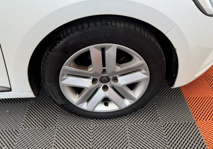 Gros plan sur la roue avant gauche blanche d'une Renault Clio Business 2021 avec jante alliage et logo Renault central.