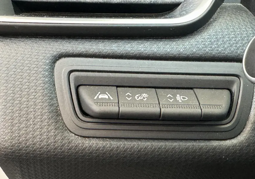 Gros plan sur les boutons de réglage d'assistance et d'éclairage du tableau de bord noir de la Renault Clio Business blanche.