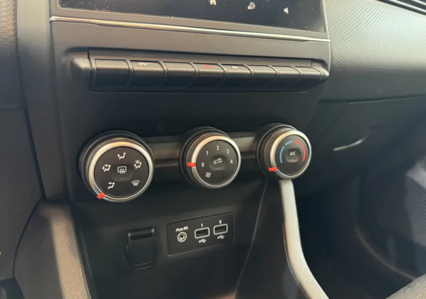 Gros plan sur les commandes de climatisation et les ports USB de la Renault Clio Business blanche, tableau de bord noir.