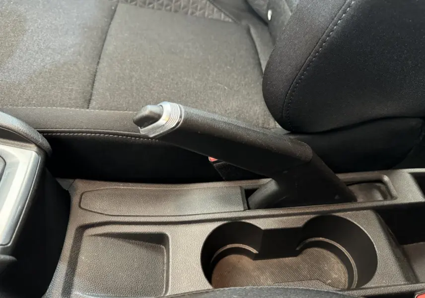 Le frein à main manuel en noir au centre de la console entre les sièges avant tissu d'une Renault Clio Business blanche.