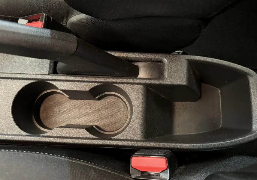 Gros plan sur la console centrale noire de la Renault Clio Business blanche, avec frein à main et porte-gobelets visibles.