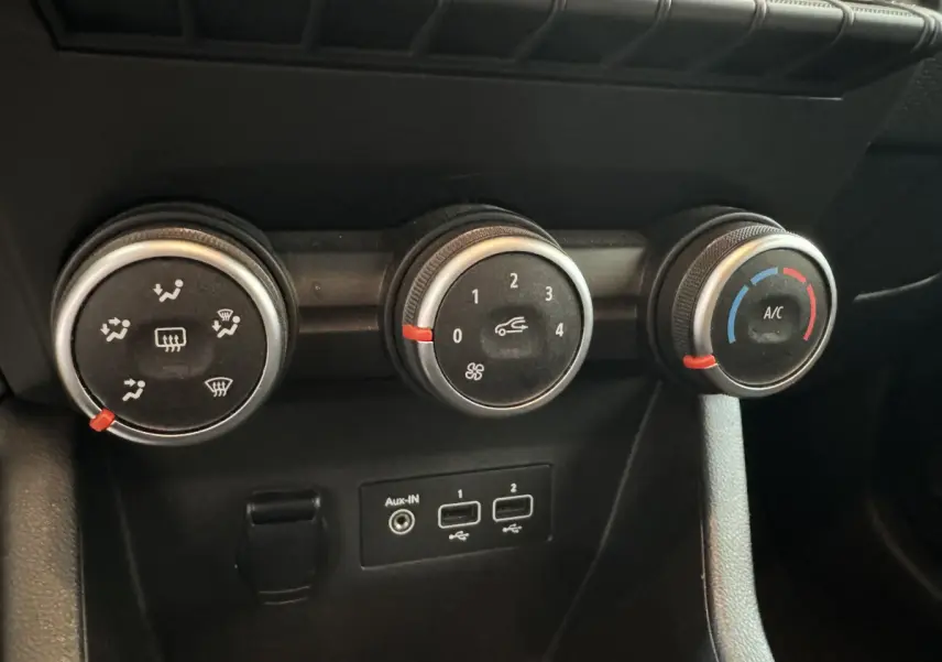 Gros plan sur les commandes de climatisation et les ports USB d'une Renault Clio Business blanche, intérieur noir.