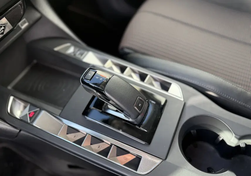 Gros plan sur la console centrale du DS3 hybride 2025, avec levier de vitesse automatique et sièges tissu gris à motifs.