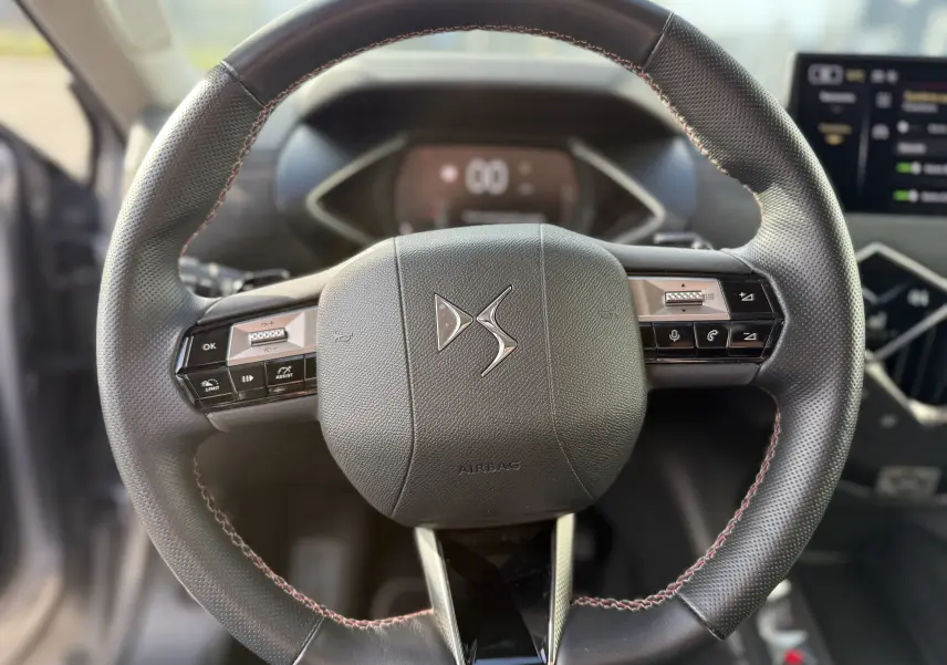 Gros plan sur le volant en cuir noir avec surpiqûres rouges du DS3 hybride 2025, mettant en valeur les commandes intégrées.