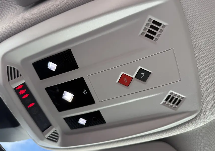 Vue en gros plan du plafonnier intérieur gris clair du DS3 2025, avec boutons SOS rouge et éclairages LED allumés.