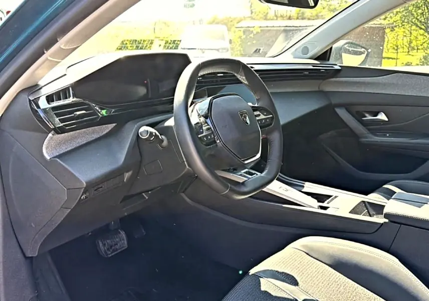 Vue intérieure côté conducteur de la Peugeot 408 Hybrid 145 allure 2025, volant cuir et tableau de bord moderne noir.