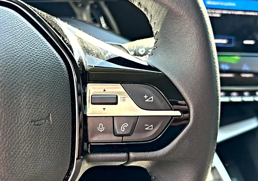 Gros plan sur les commandes vocales et téléphone au volant cuir noir du Peugeot 408 Hybrid 145 allure 2025.