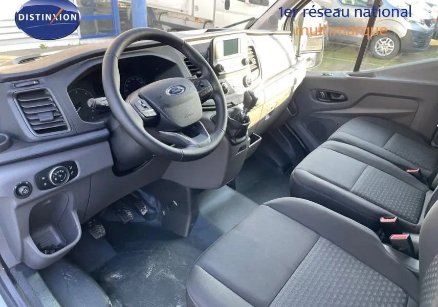 Intérieur du Ford Transit Fourgon blanc 2023 vu côté conducteur, montrant tableau de bord et sièges noirs.