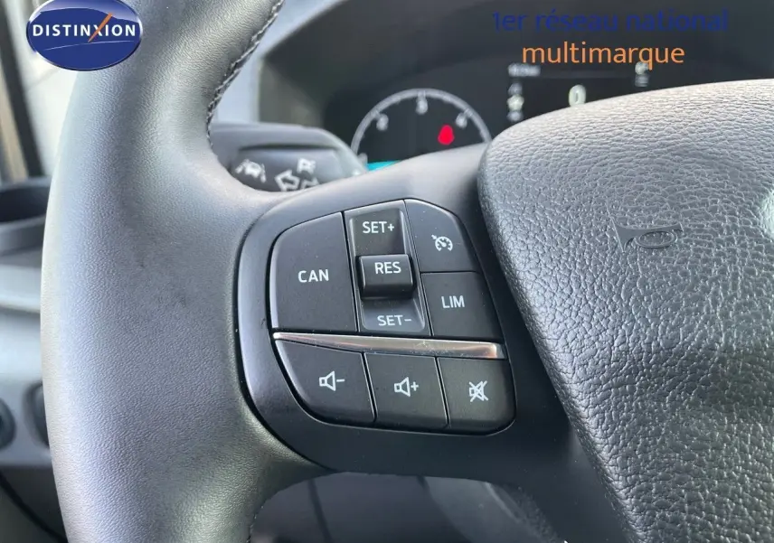 Gros plan sur les commandes de régulateur et volume au volant noir du Ford Transit Fourgon blanc 2023.