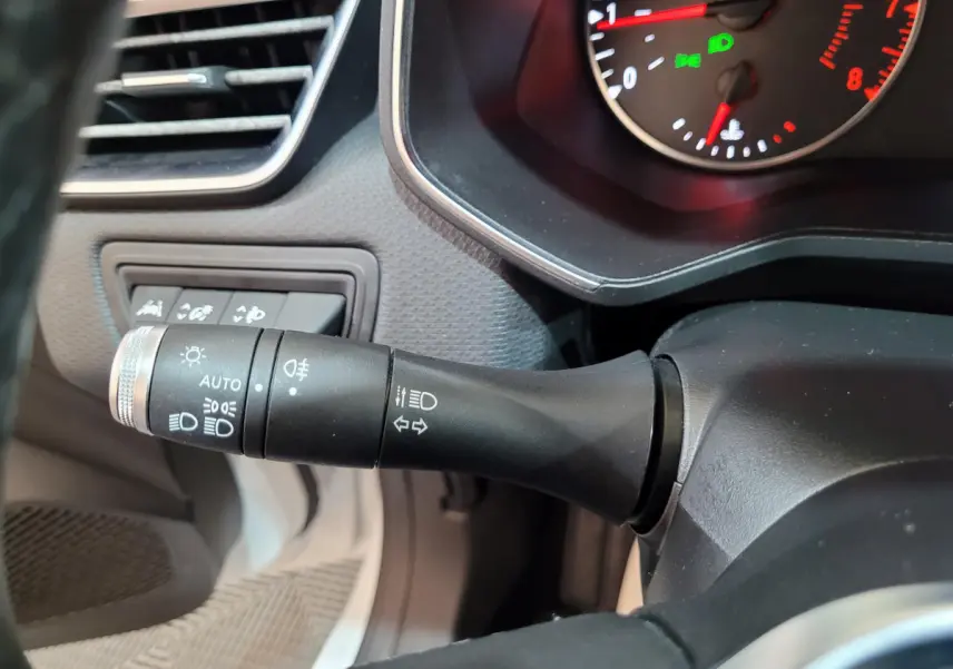 Gros plan sur la manette des feux à gauche du volant dans l'habitacle d'une Renault Clio Business blanche de 2021.