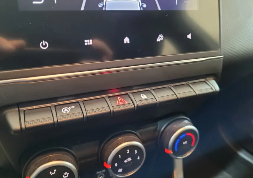 Gros plan sur la console centrale de la Renault Clio Business blanche, montrant les commandes de climatisation et les boutons d'alerte.