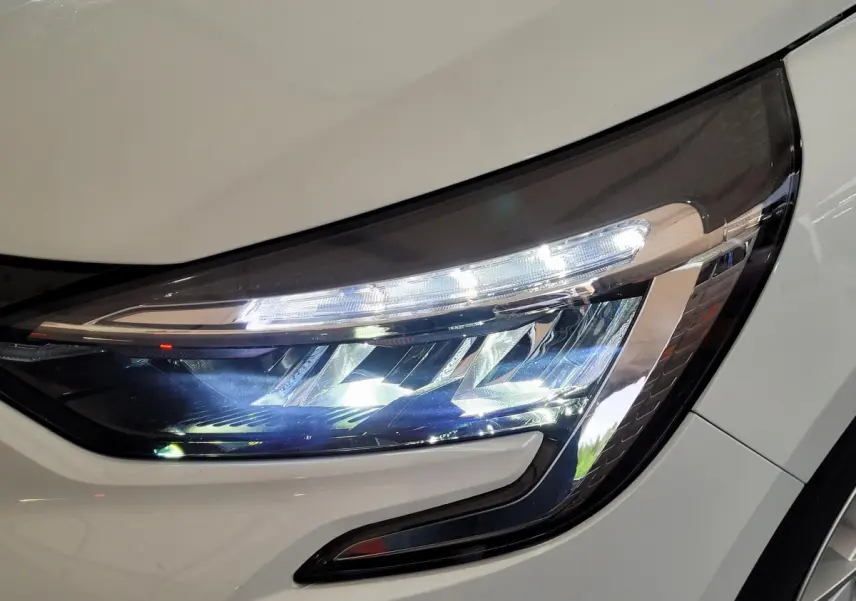 Gros plan sur le phare avant droit allumé d'une Renault Clio Business blanche de 2021, soulignant son design LED distinctif.