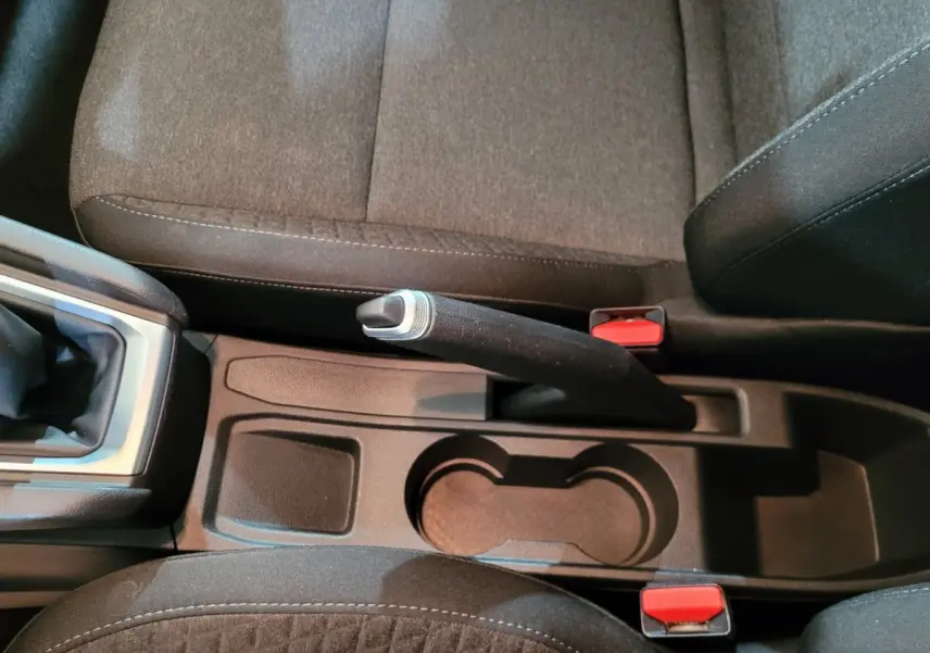 Vue rapprochée de la console centrale noire de la Renault Clio Business blanche, avec frein à main manuel et porte-gobelets.