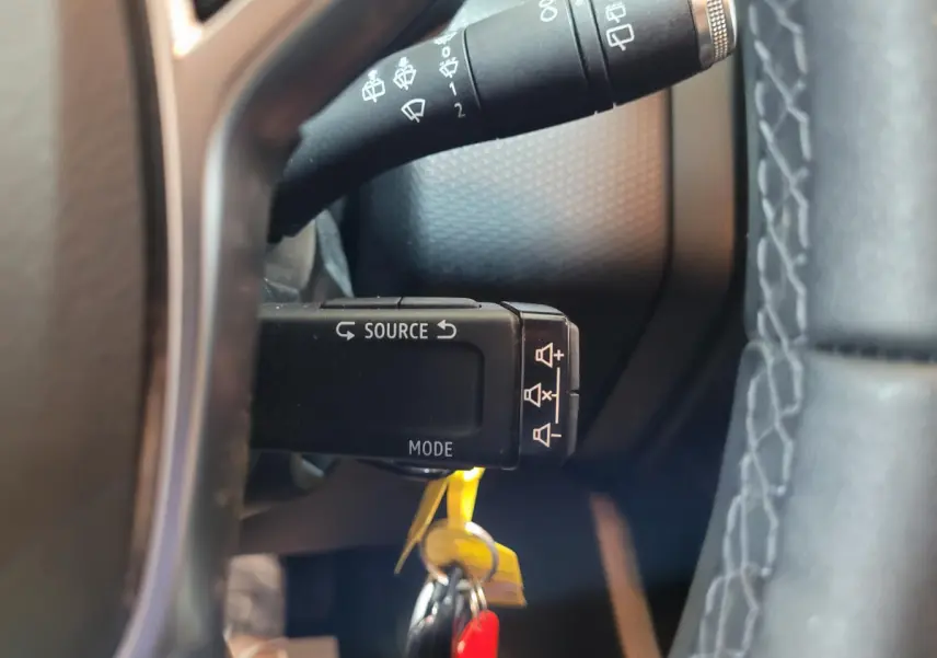 Gros plan sur la commande multimédia au volant d'une Renault Clio Business blanche, avec clé insérée et volant cuir visible.