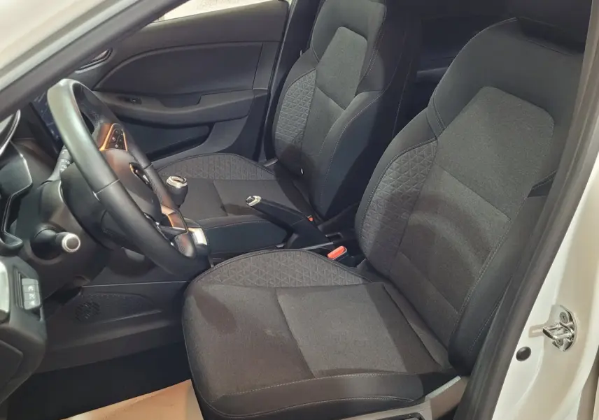 Vue intérieure côté conducteur de la Renault Clio Business blanche, sièges noirs et volant cuir synthétique visible.