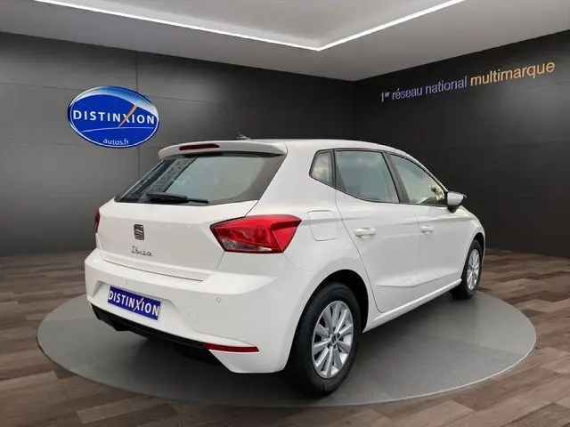 Vue 3/4 arrière droite d'une SEAT Ibiza blanc candy 2023, compacte cinq portes avec feux arrière LED distinctifs.