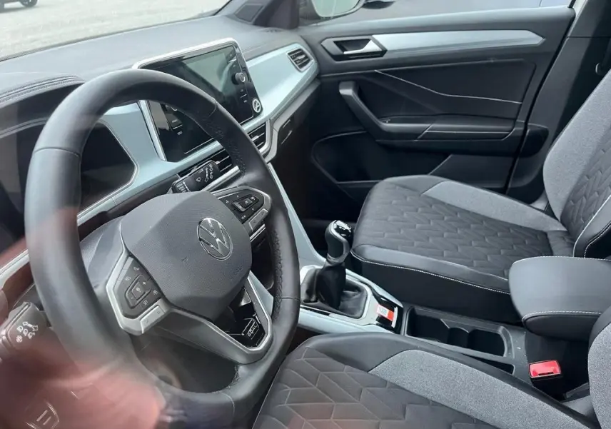 Vue intérieure côté conducteur du Volkswagen T-Roc 2025, avec volant multifonction et sièges tissu gris à motifs géométriques.