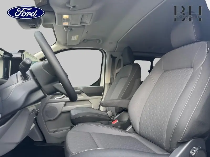 Intérieur du Ford Transit Custom Fourgon 2026, vue côté conducteur montrant les sièges gris et le volant noir.