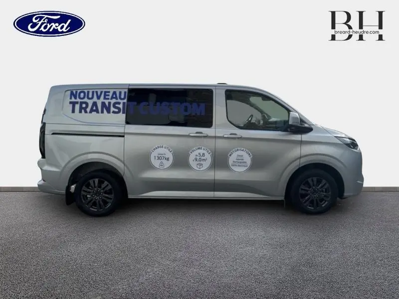 Vue latérale droite du Ford Transit Custom Fourgon gris lunaire métallisé avec marquages publicitaires sur la carrosserie.