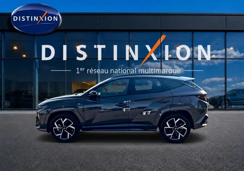 Vue de profil droit du Hyundai Tucson gris écotronique avec jantes alliage 19 et détails N Line devant une vitrine Distinxion.