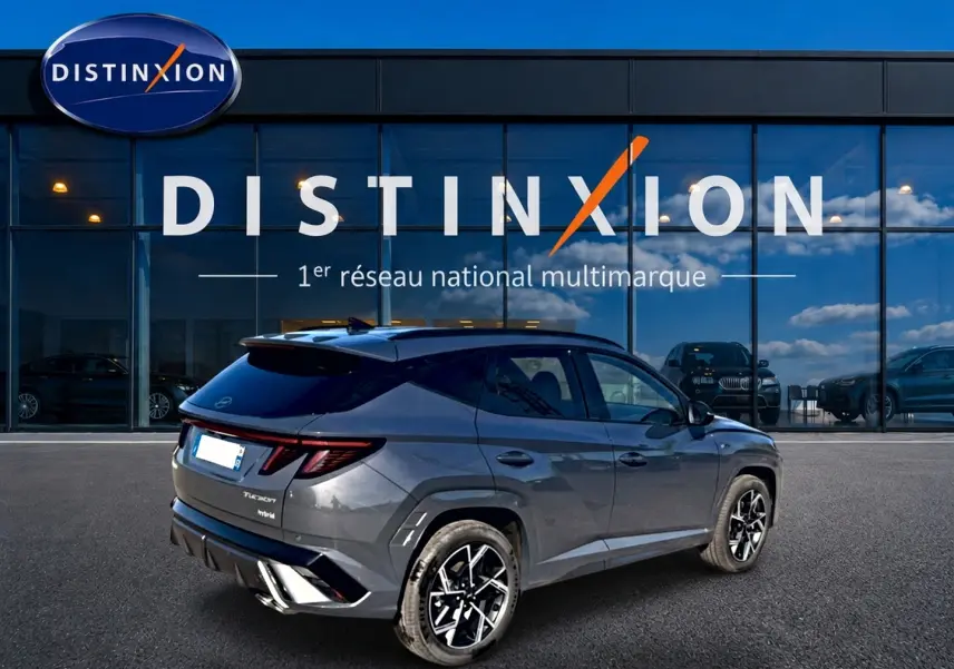 Vue 3/4 arrière droite du Hyundai Tucson 2026 gris ecotronique avec jantes alliage et toit noir devant une vitrine Distinxion.