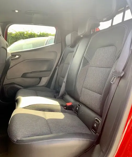 Vue latérale intérieure des sièges arrière en tissu et cuir d'une Renault Clio V rouge 2021, avec ceinture de sécurité visible.