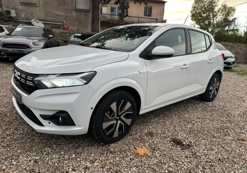 Vue 3/4 avant droite d'une Dacia Sandero TCe 90 Expression blanche avec jantes noires et phares allumés.