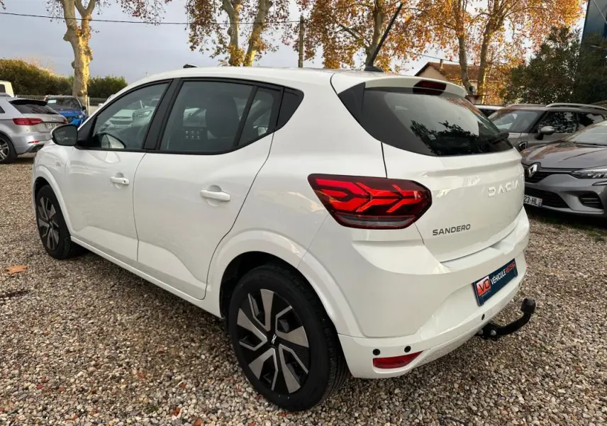 Vue 3/4 arrière droite d'une Dacia Sandero blanche 2024 avec feux arrière LED et attelage de remorque.