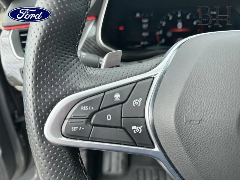 Gros plan sur le volant cuir perforé côté gauche avec commandes de régulateur sur Renault Arkana gris métallisé.