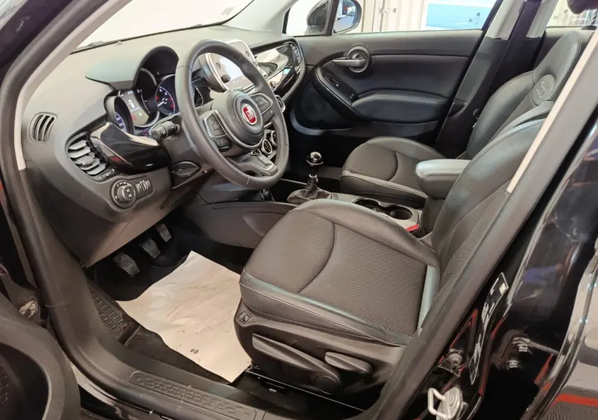 Vue intérieure côté conducteur de la Fiat 500X 2020, sièges noirs, volant multifonctions et levier de vitesse manuel visibles.