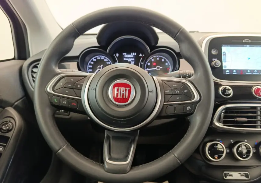 Vue intérieure centrée sur le volant noir cuir du Fiat 500X avec tableau de bord et écran tactile navigation visible à droite.
