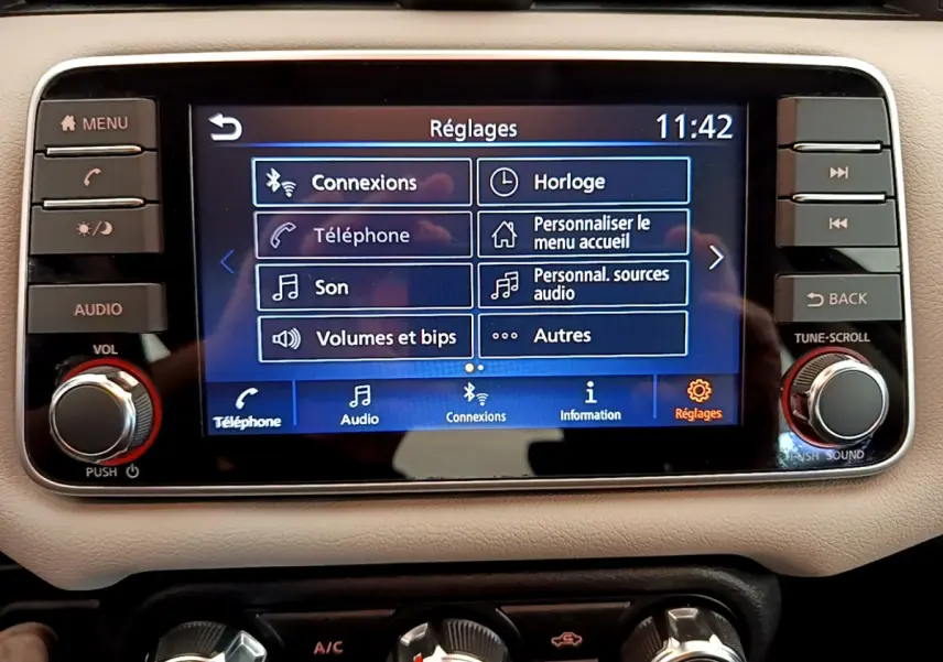 Écran tactile central affichant les réglages audio et connexions dans le tableau de bord beige d'une Nissan Micra blanche