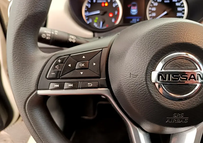 Gros plan sur le volant noir de la Nissan Micra 2022 avec commandes multifonctions et tableau de bord éclairé.