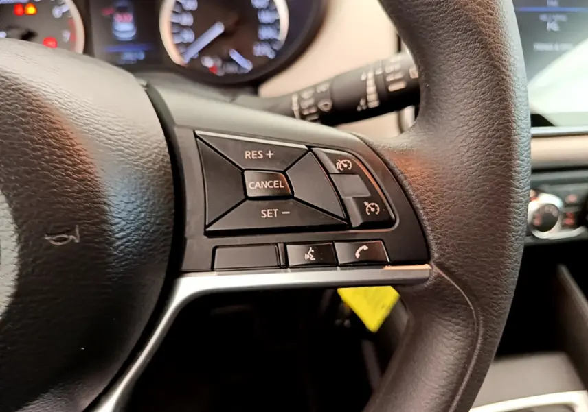 Gros plan sur les commandes du volant noir de la Nissan Micra IG-T 92 Acenta 2022, avec tableau de bord flou en arrière-plan.