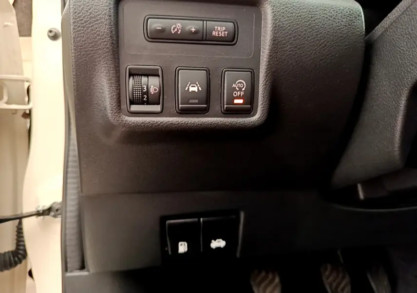 Vue rapprochée des commandes de réglage des phares et d'assistance sur le tableau de bord gauche d'une Nissan Micra blanche 2022.