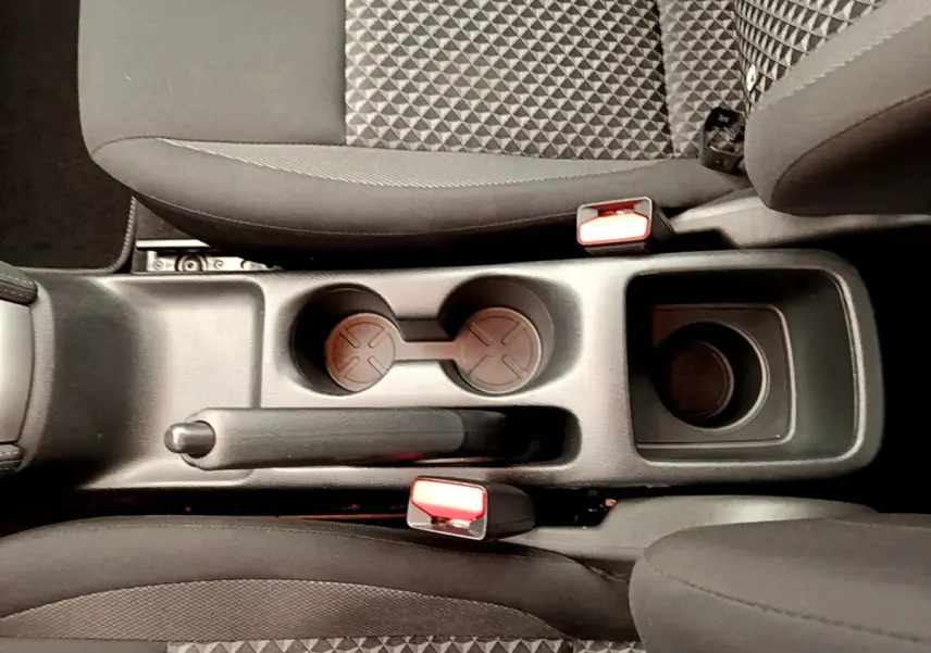 Vue plongeante sur la console centrale noire avec frein à main et porte-gobelets entre les sièges tissu gris de la Nissan Micra 2022.