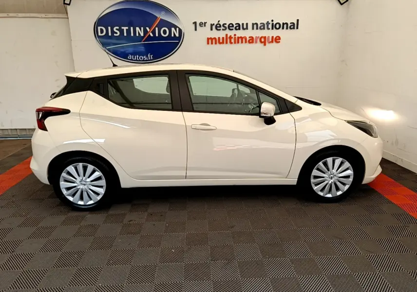 Profil côté droit d'une Nissan Micra blanche 2022 Acenta dans un showroom avec logo Distinxion en arrière-plan.