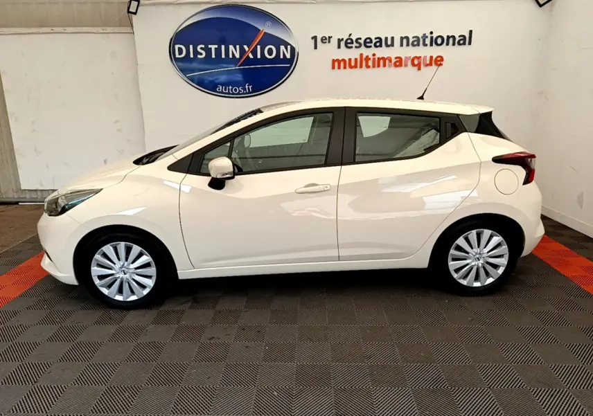 Profil latéral gauche d'une Nissan Micra blanche 2022 en intérieur, avec jantes alliage et toit noir contrastant.